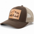 A brown and beige fishing cap with a Sasquatch patch on the front featuring mountain and tree graphics.
