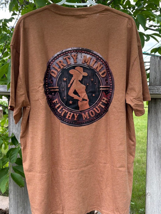 Brown t-shirt with graphic design hanging on a wooden fence with greenery in the background