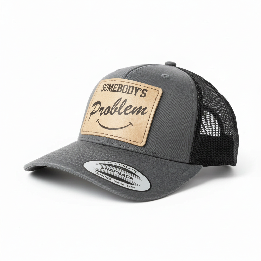 Gray and black trucker cap with leather patch and 'Somebody's Problem' text on a white background