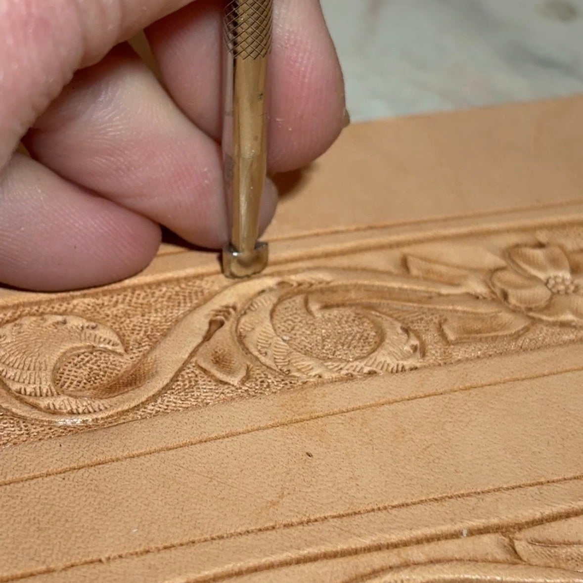 Hand holding a chisel and carving intricate patterns into leather